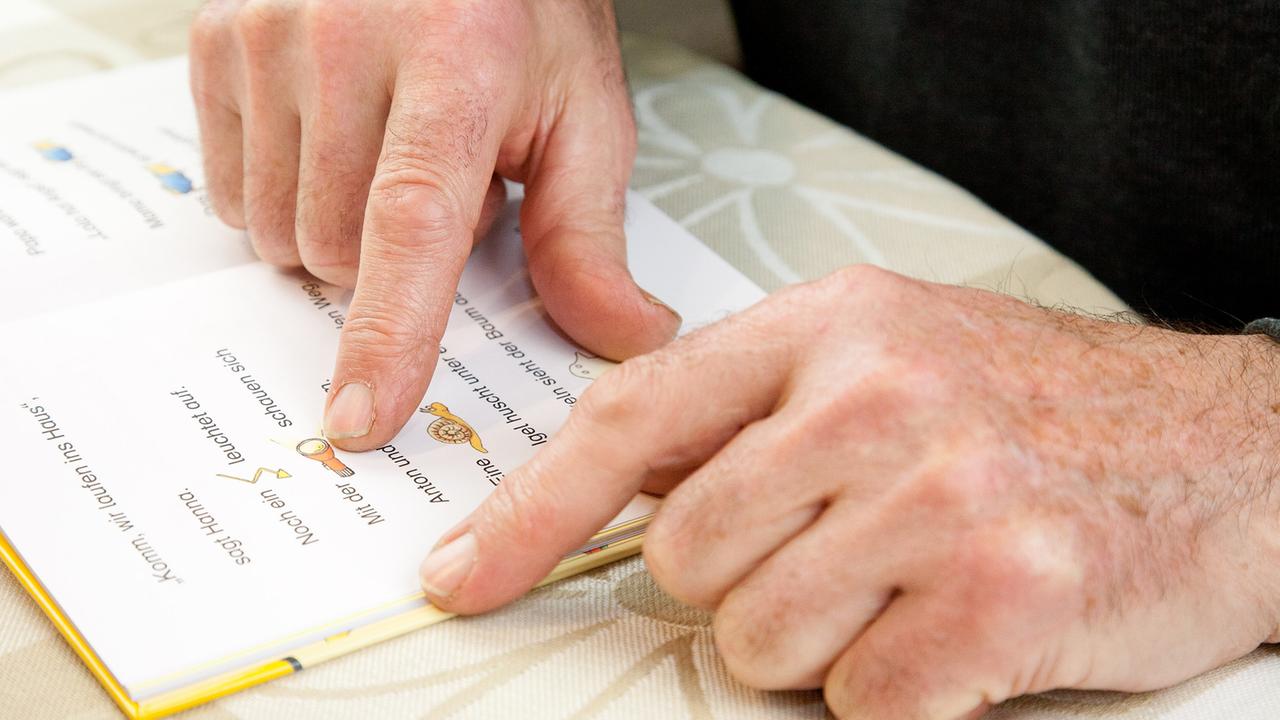 Die Finger eines älteren Mannes gleiten über die Zeilen eines Buches für Leseanfänger.