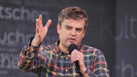 Matthias Nawrat sitzt in einem karierten Hemd in Leipzig, Sachsen, au der Bühne und spricht. Matthias Nawrat sitzt in einem karierten Hemd in Leipzig, Sachsen, au der Bühne und spricht.