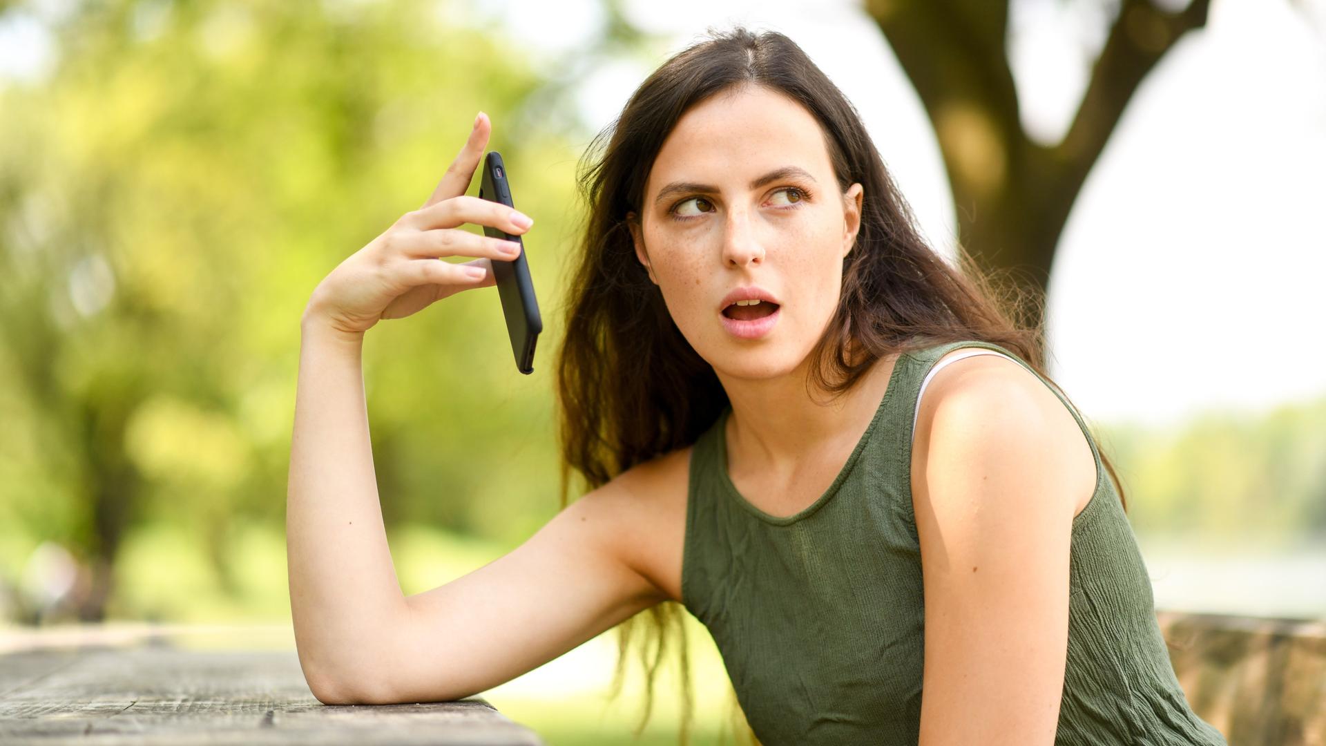 Frau hält genervt Handy vom Ohr.