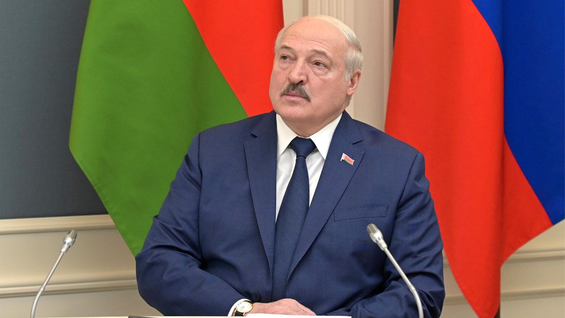 Belarus' Präsident Lukaschenko sitzt an einem Pult mit Mikrofonen. Er hält die Hände gefaltet.