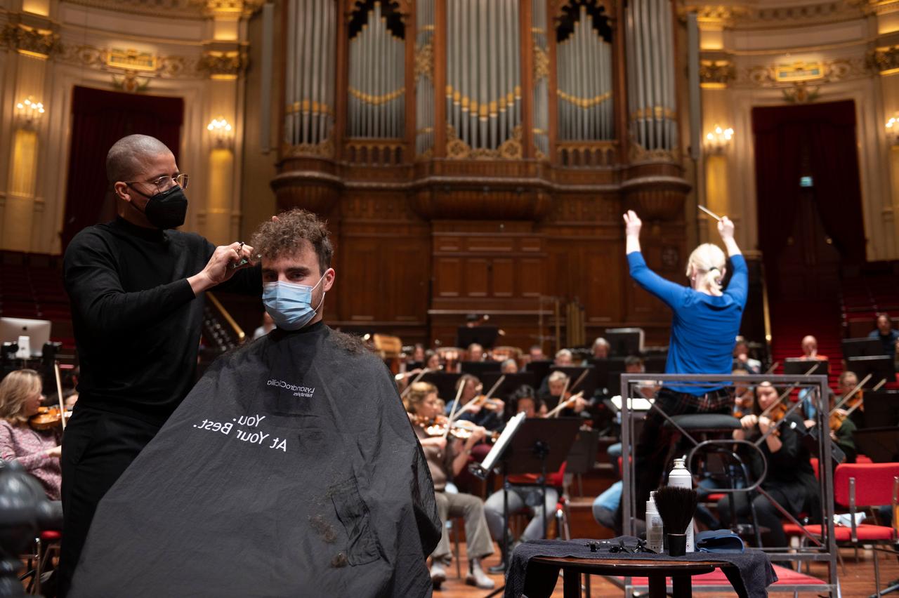 In der Amsterdamer Philharmonie - dem Concertgebouw - lässt sich ein Besucher während eines Konzerts die Haare schneiden. Im Hintergrund sind die Orchestermusiker zu sehen.