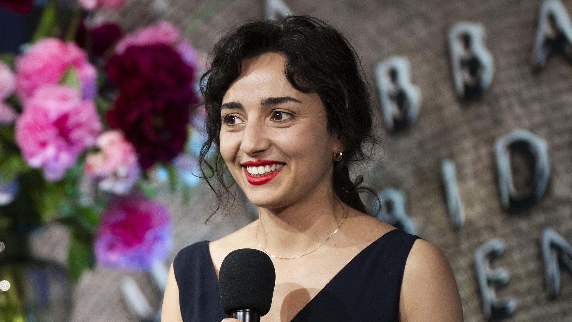 Porträt der niederländischen Schriftstellerin Safae el Khannoussi. Die junge Frau steht im Rahmen einer Preisverleihung im schwarzen Kleid auf einer Bühne.