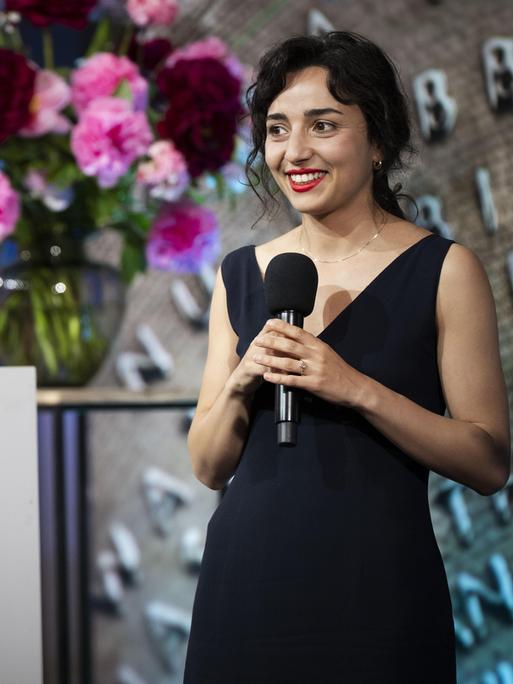 Porträt der niederländischen Schriftstellerin Safae el Khannoussi. Die junge Frau steht im Rahmen einer Preisverleihung im schwarzen Kleid auf einer Bühne.