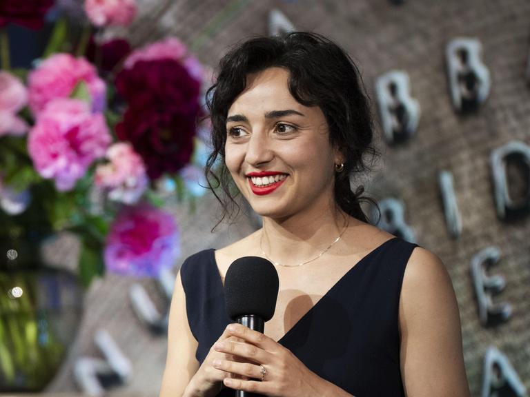 Porträt der niederländischen Schriftstellerin Safae el Khannoussi. Die junge Frau steht im Rahmen einer Preisverleihung im schwarzen Kleid auf einer Bühne.