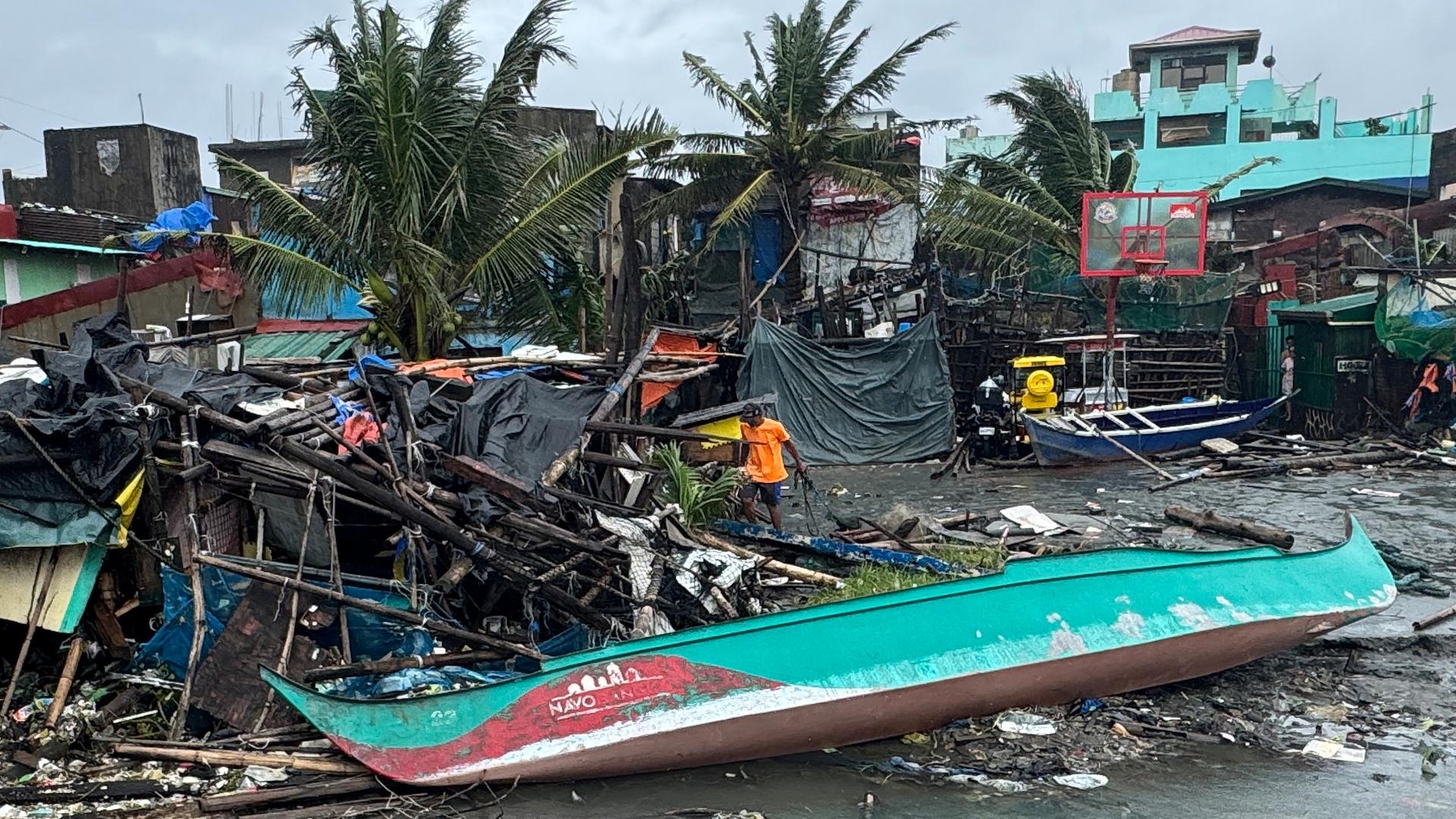 Zerstörte Häuser, Schutt, Matsch und Habseligkeiten liegen neben einem Holzboot. 