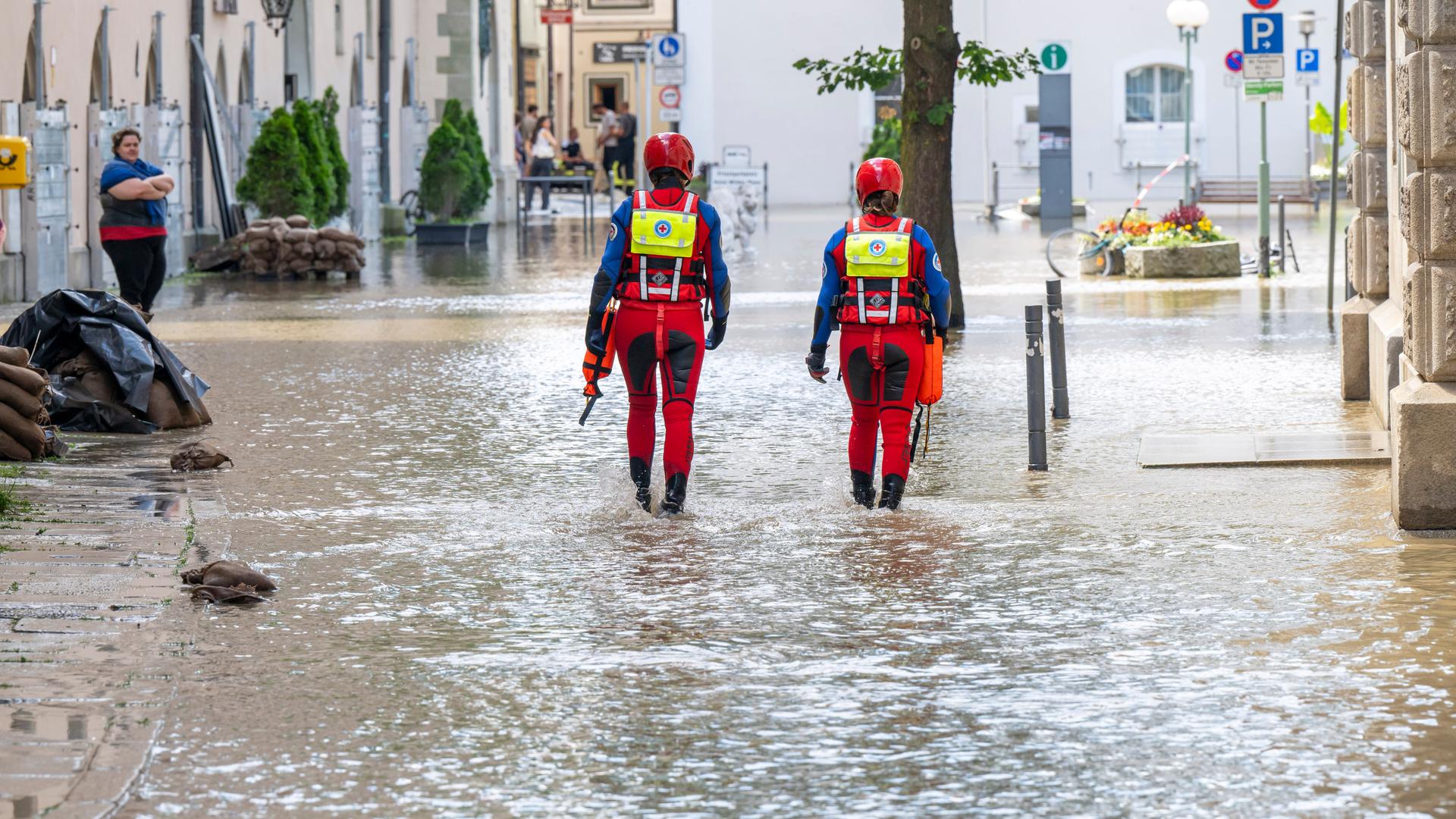 Mitarbeiter der Wasserwacht waten durch eine Gasse an der Dreiflüssestadt. In Bayern herrscht nach heftigen Regenfällen vielerorts weiter Land unter.