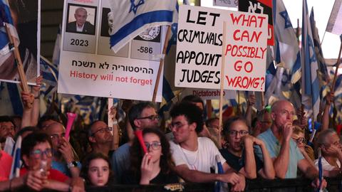 Demonstranten halten Plakate hoch, auf denen Ministerpräsident Netanjahu und seine Regierung kritisiert werden. Die Menschen schwenken außerdem israelische Flaggen.