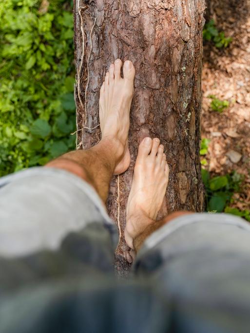 Ein Mann balanciert barfuß über einen Baumstamm. (Symbolfoto)