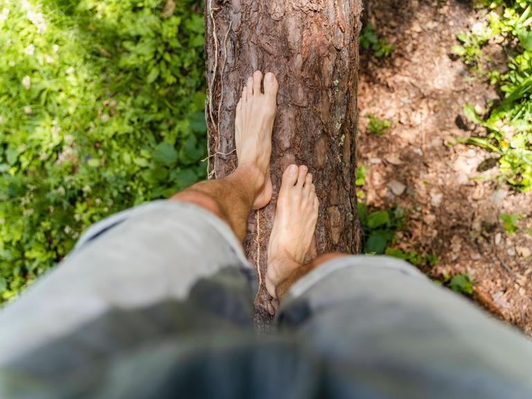 Ein Mann balanciert barfuß über einen Baumstamm. (Symbolfoto)