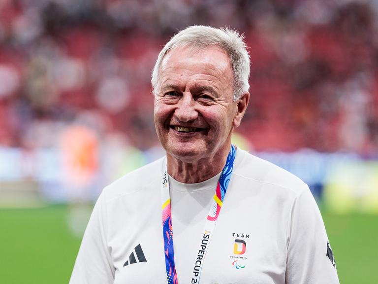 Friedhelm Julius Beucher trägt Sportkleidung und steht in einem Stadion.