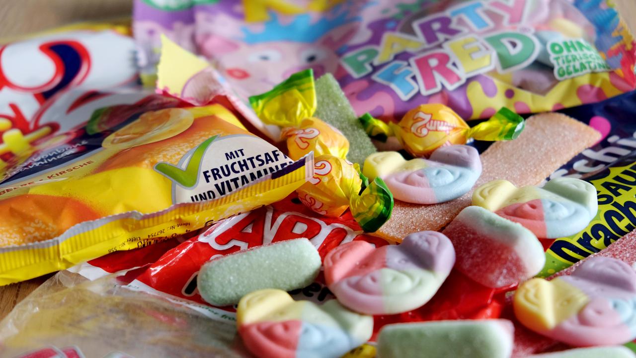 Zu sehen sind bunte Gummibärchen mit Tier-Gesichtern und Süßigkeiten-Verpackungen mit knalligen Farben. 