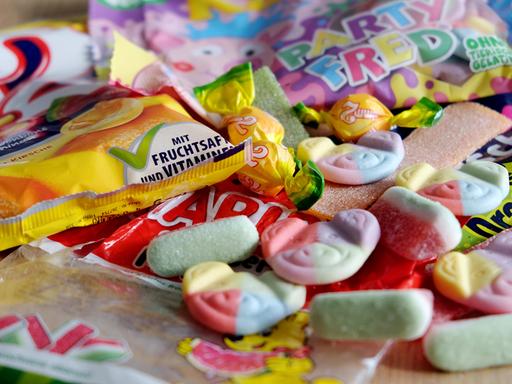 Zu sehen sind bunte Gummibärchen mit Tier-Gesichtern und Süßigkeiten-Verpackungen mit knalligen Farben. 