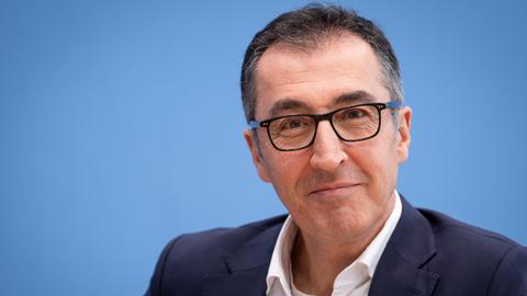 Cem Özdemir sitzt vor einem blauen Hintergrund und blickt in die Kamera.