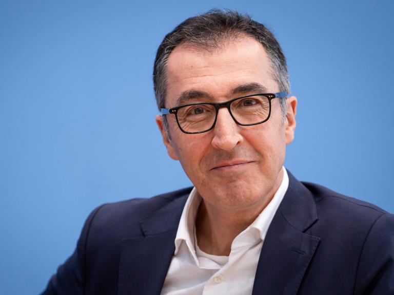 Cem Özdemir sitzt vor einem blauen Hintergrund und blickt in die Kamera.