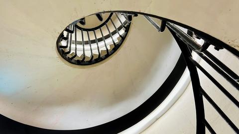 Ausschnitte einer Wendeltreppe mit schwarzen Handläufen vor weißem Grund