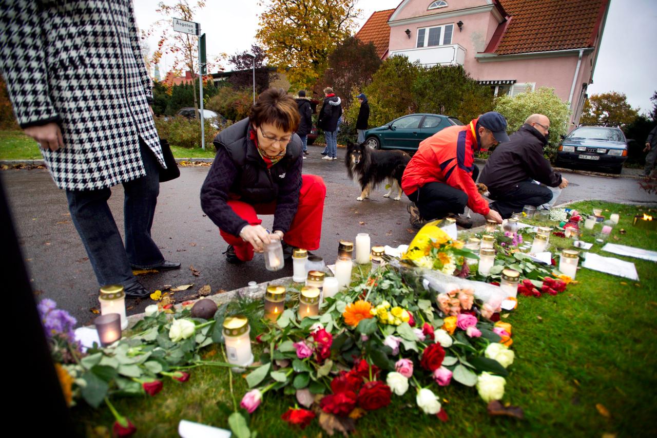 Menschen legen Blumen nieder und zünden Kerzen in einer Wohnsiedlung an.