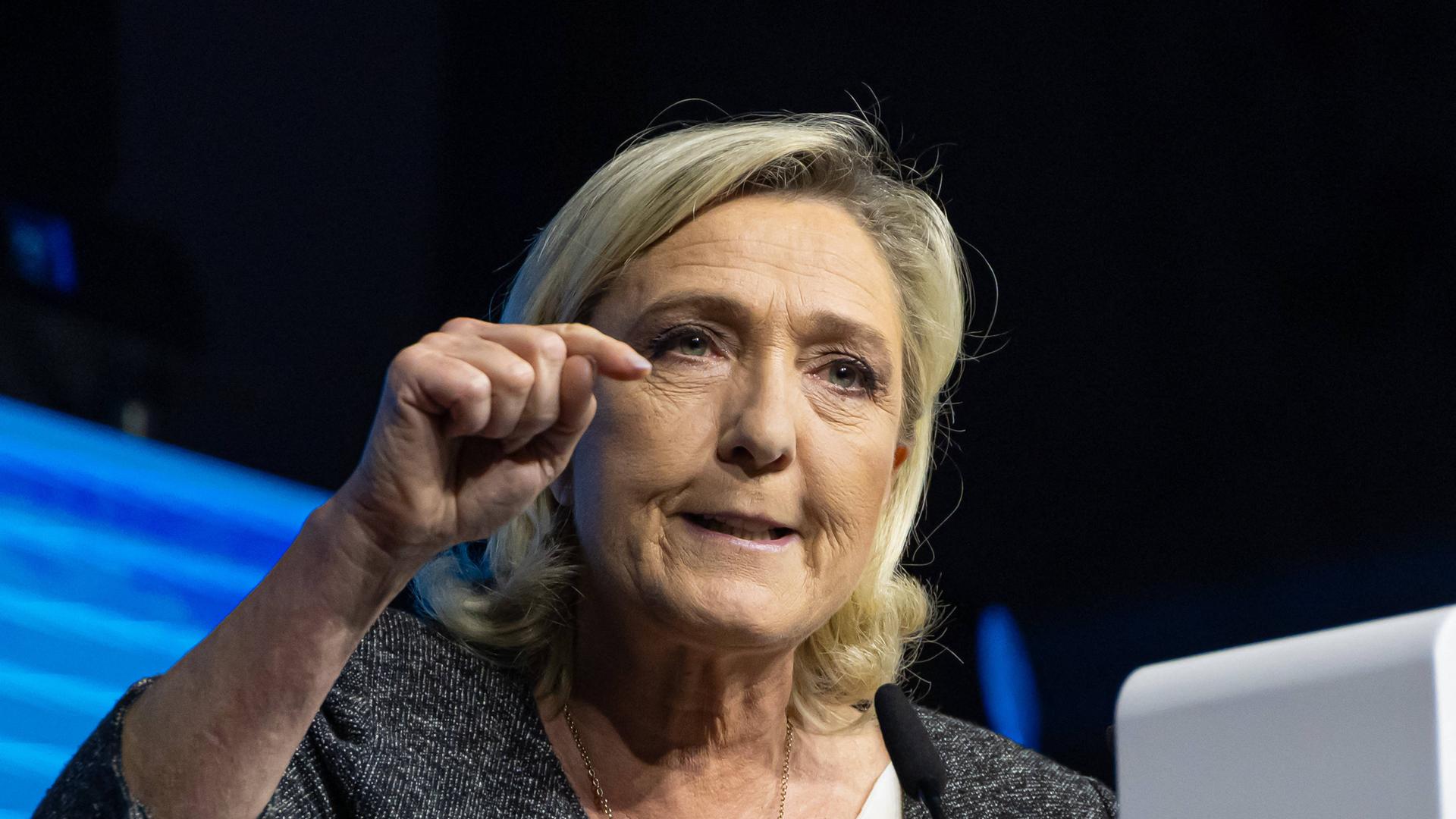 Die französische Politikerin Marine Le Pen steht auf einer Bühne. Sie guck verbissen in die Menge und zeigt mit einem Finger auf sie.