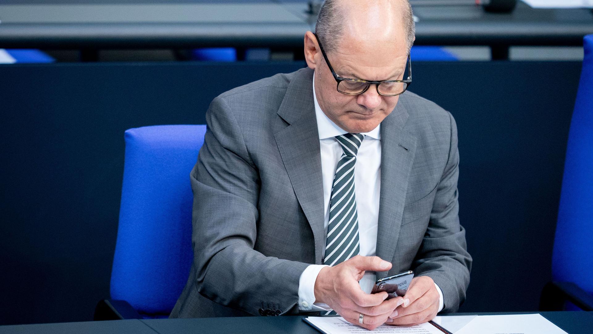 Olaf Scholz sitzt auf seinem Platz im Bundestag und schaut in sein Handy