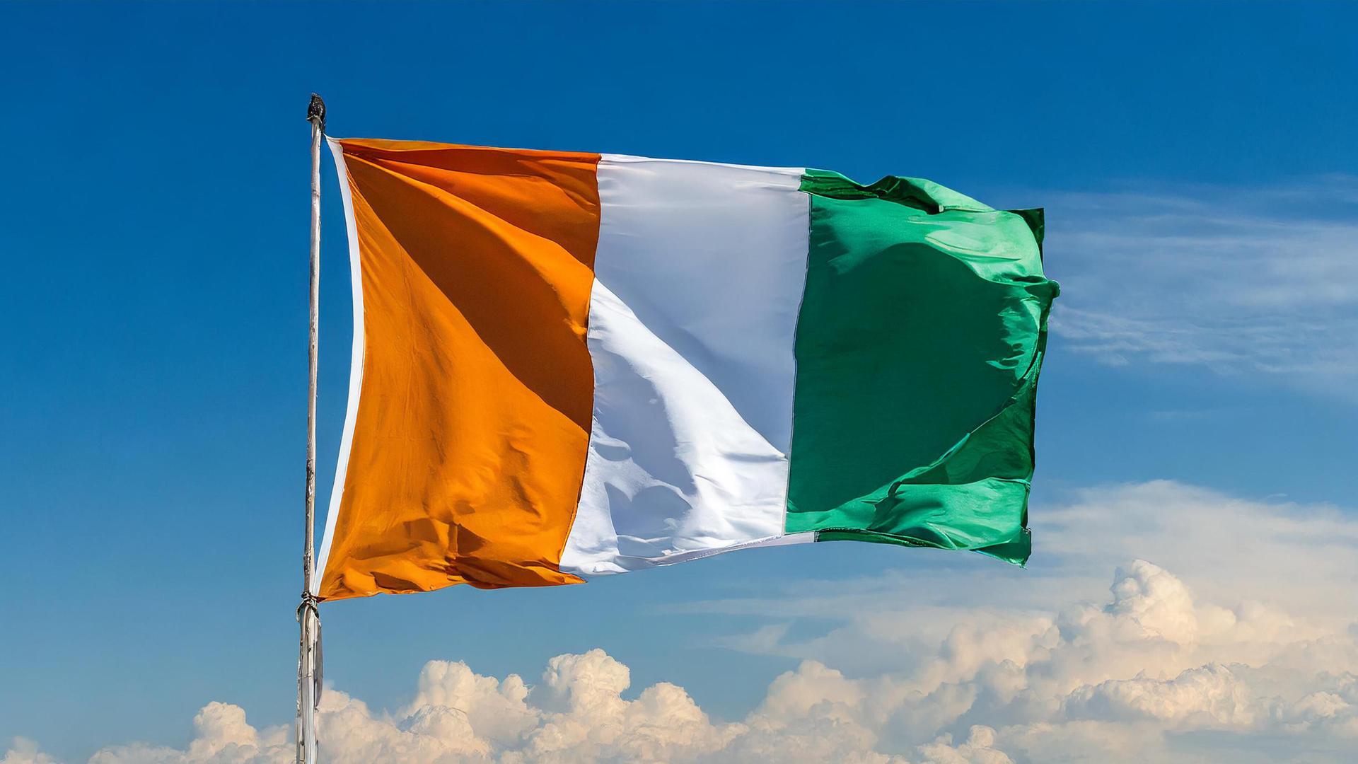Die Flagge der Elfenbeinküste weht im Wind vor blauem Himmel Die Flagge der Elfenbeinküste weht im Wind vor blauem Himmel
