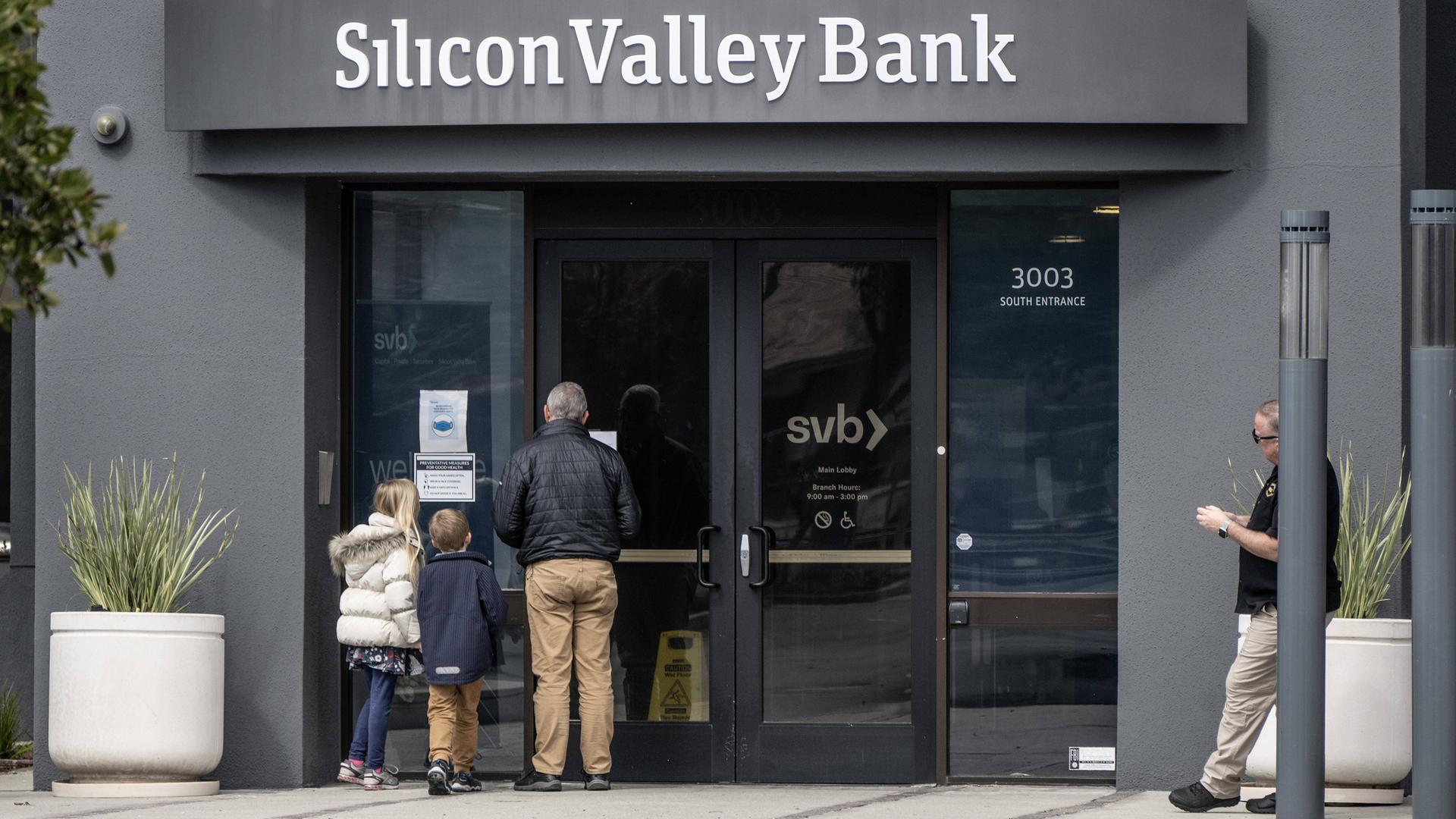 Vor einer Filiale der Silicon Valley Bank lesen ein älterer Mann und zwei Kinder eine an der Tür ausgehängte Bekanntmachung.