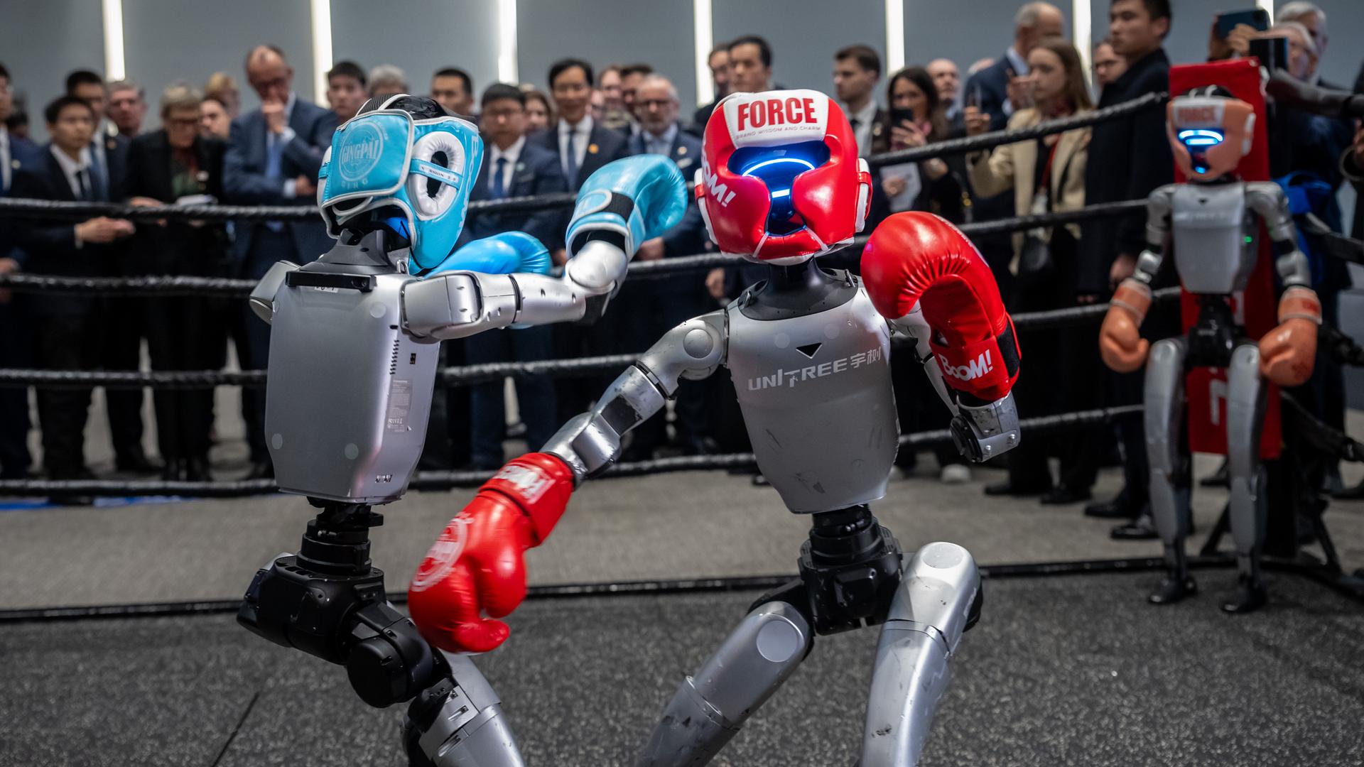 Zwei Roboter boxen während dahinter Bundeskanzler Friedrich Merz (CDU) die Firma Unitree Robotics in der Provinz Zhejiang besucht. 