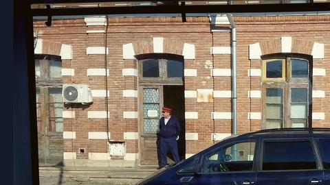 Ein Bahnhof in Rumänien aus einem Zugfenster heraus fotografiert. Zu sehen ist ausserdem ein Schaffner der vor der Türe des Bahnwärterhäuschen steht.