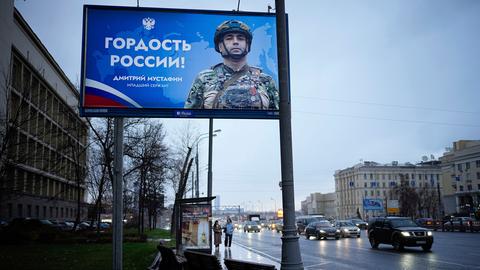 Zwei Frauen gehen unter einem großen Werbeplakat für das russische Militär lang.