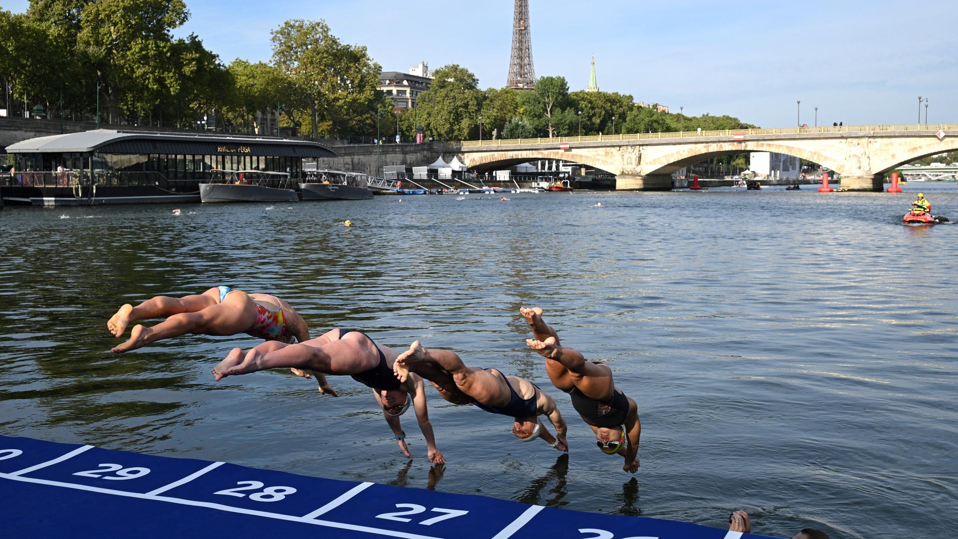 Mehrere Schwimmerinnen springen von einem Startpunkt in einen Fluss. Mehrere Schwimmerinnen springen von einem Startpunkt in einen Fluss.