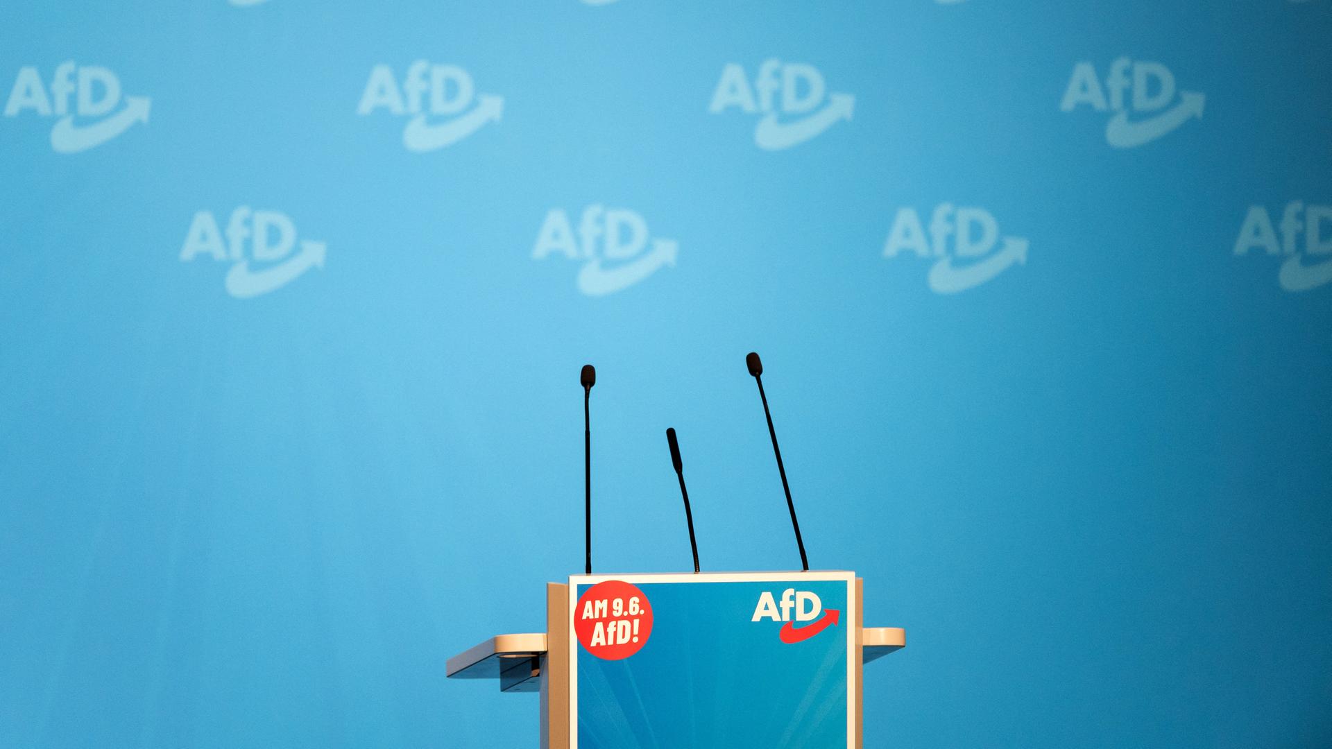 Ein leeres Rednerpult auf der Bühne des Vorbereitungstreffens der AfD für die Europawahl. Im Hintergrund sieht man Parteilogos auf einer blauen Wand.