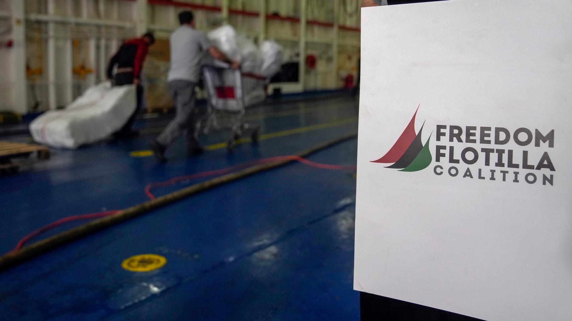 Das Foto zeigt einen Arbeiter, der Hilfsgüter in ein Schiff bringt. Im Vordergrund ist das Logo der Hilfsorganisation "Freedom Flotilla Coalition" zu sehen (Archivfoto vom 19. April 2024).
