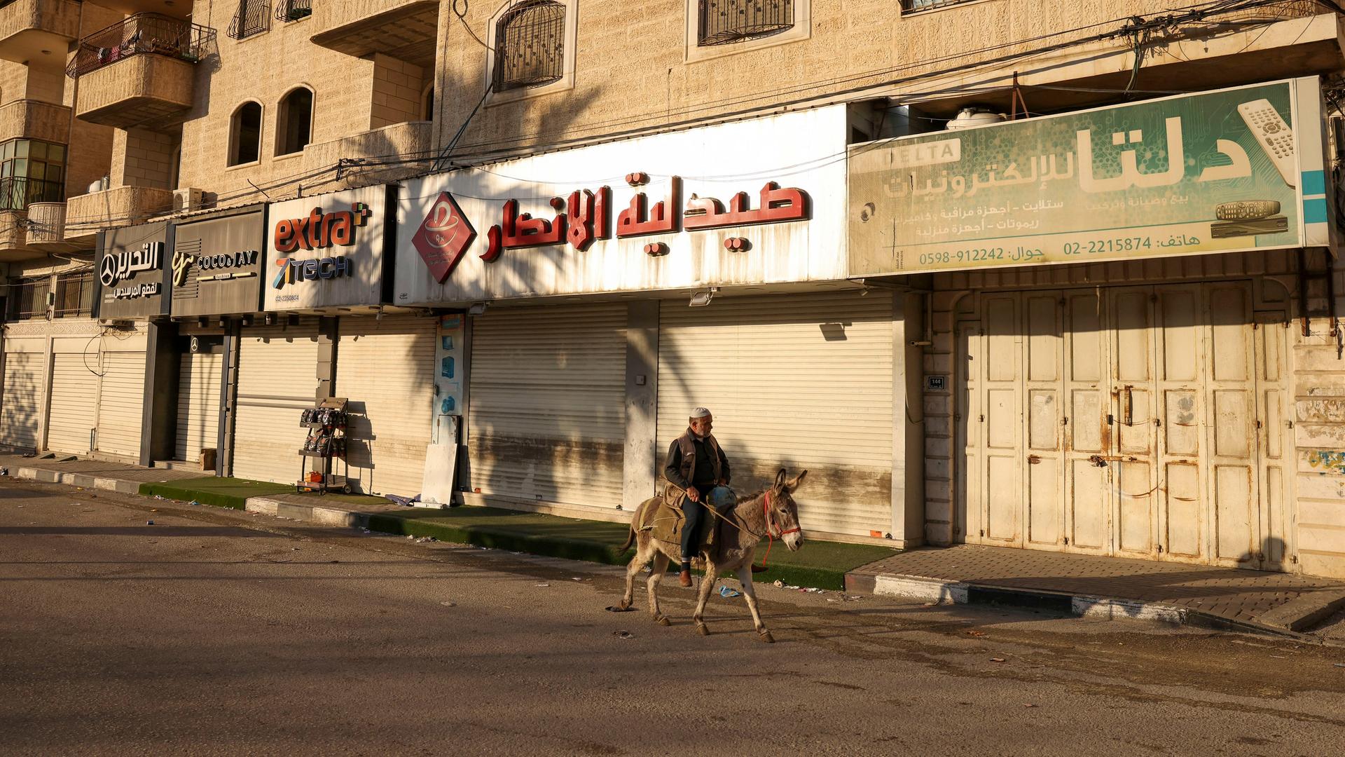 Eine Straße in Hebron, in der alle Geschäfte geschlossen sind. Nur ein Mann auf einem Esel reitet an ihnen vorbei.