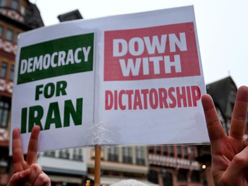 Demonstranten halten ein Schild hoch, auf dem steht: "democracy for iran" und "down with dictatorship".