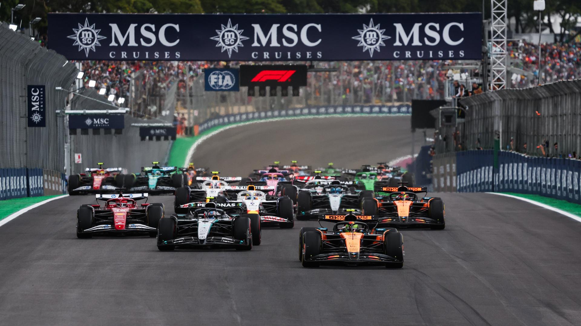 Mehrere Formel-1-Rennwagen stehen auf der Rennstrecke beim Start zum Großen Preis von Sao Paulo. Im Hintergrund befinden sich Zuschauer hinter Absperrungen. Mehrere Formel-1-Rennwagen stehen auf der Rennstrecke beim Start zum Großen Preis von Sao Paulo. Im Hintergrund befinden sich Zuschauer hinter Absperrungen.