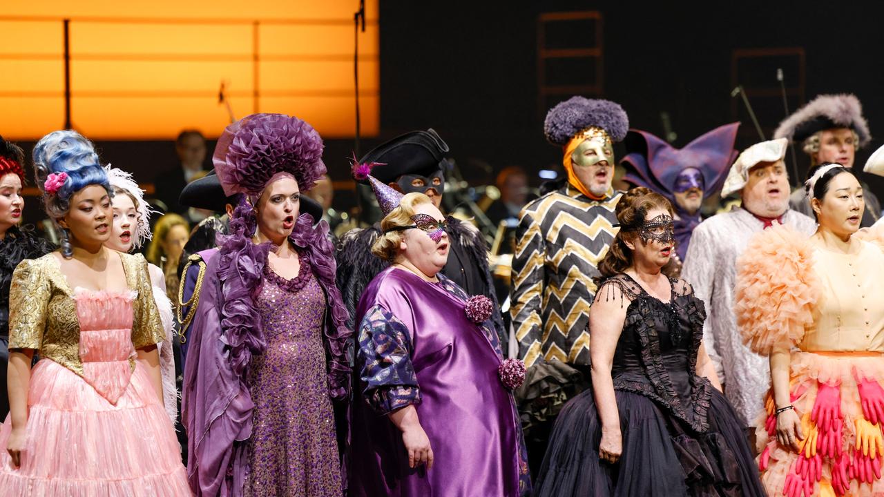Der Chor der Oper Köln singt in bunten Kostümen auf der Bühne.
