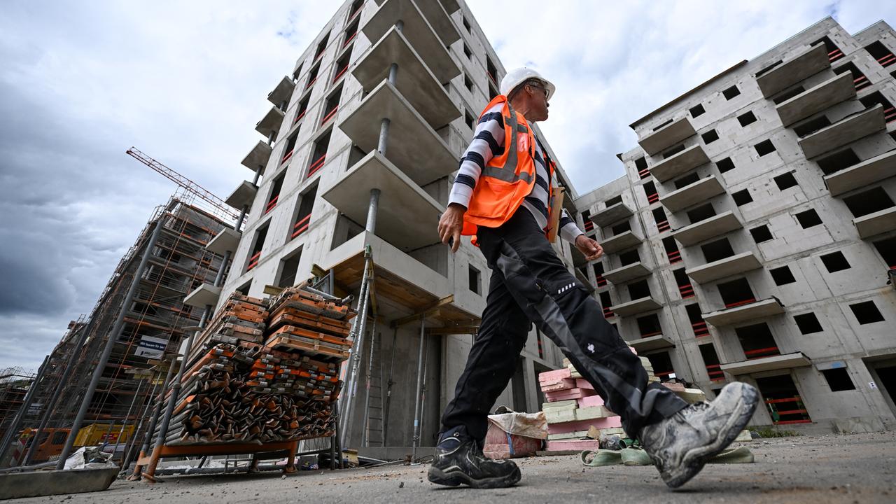 Ein Bauarbeiter in Warnweste und Helm läuft über die Baustelle eines Apartment-Komplexes. Ein Bauarbeiter in Warnweste und Helm läuft über die Baustelle eines Apartment-Komplexes.