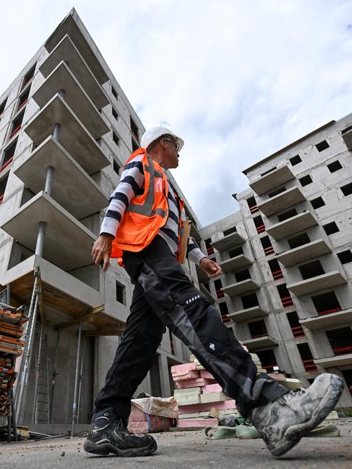 Ein Bauarbeiter in Warnweste und Helm läuft über die Baustelle eines Apartment-Komplexes.