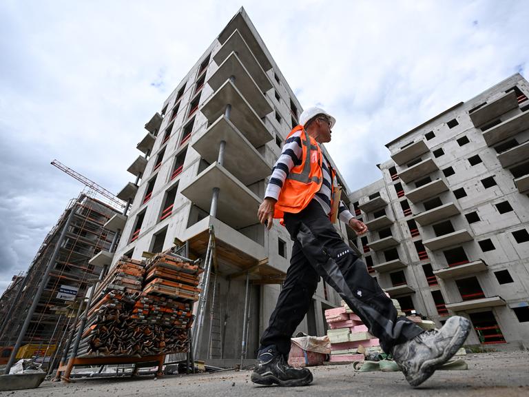 Ein Bauarbeiter in Warnweste und Helm läuft über die Baustelle eines Apartment-Komplexes.