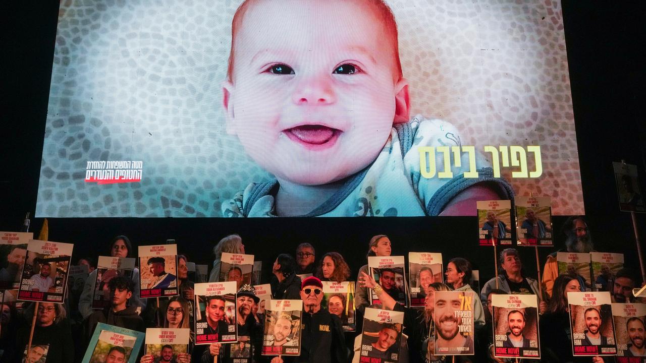 Demonstrierende halten Schilder mit den Gesichtern und Namen der israelischen Geiseln in die Luft. Darüber ist ein Baby auf einer Leinwand zu sehen.