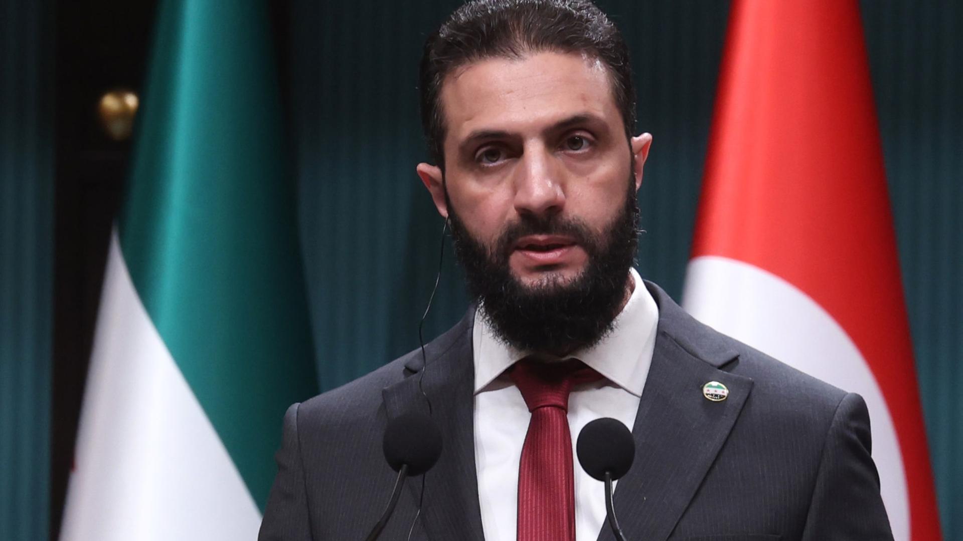 Ahmed al-Sharaa, der neue Machthaber in Syrien, steht während einer Pressekonferenz hinter einem Sprechpult. Dahinter die syrische und die türkische Flagge.