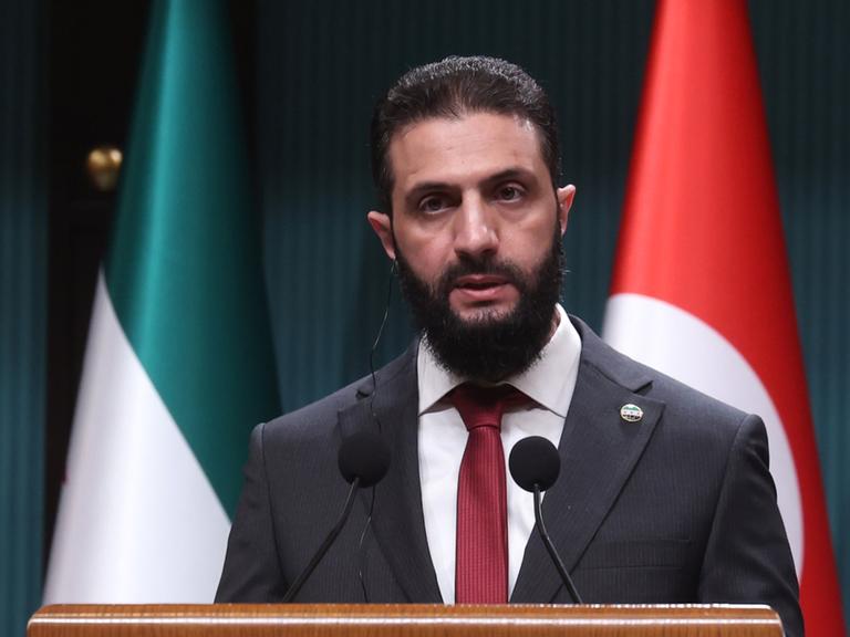 Ahmed al-Sharaa, der neue Machthaber in Syrien, steht während einer Pressekonferenz hinter einem Sprechpult. Dahinter die syrische und die türkische Flagge.