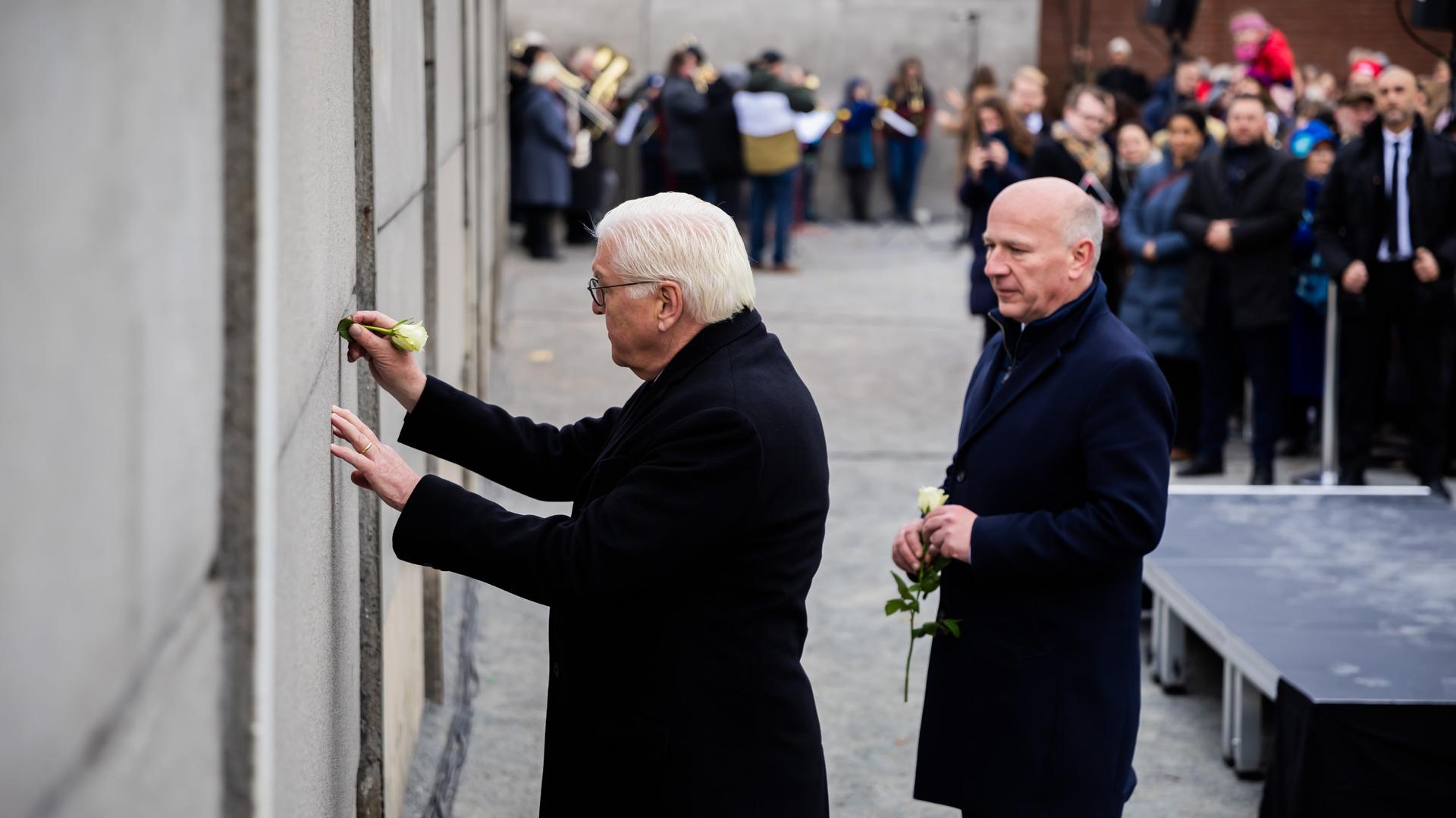 Bundespräsident Frank-Walter Steinmeier (l) steckt bei einer zentralen Gedenkveranstaltung anlässlich von 35 Jahre friedliche Revolution und Mauerfall in der Gedenkstätte Berliner Mauer eine Rose in die Hinterlandmauer. 