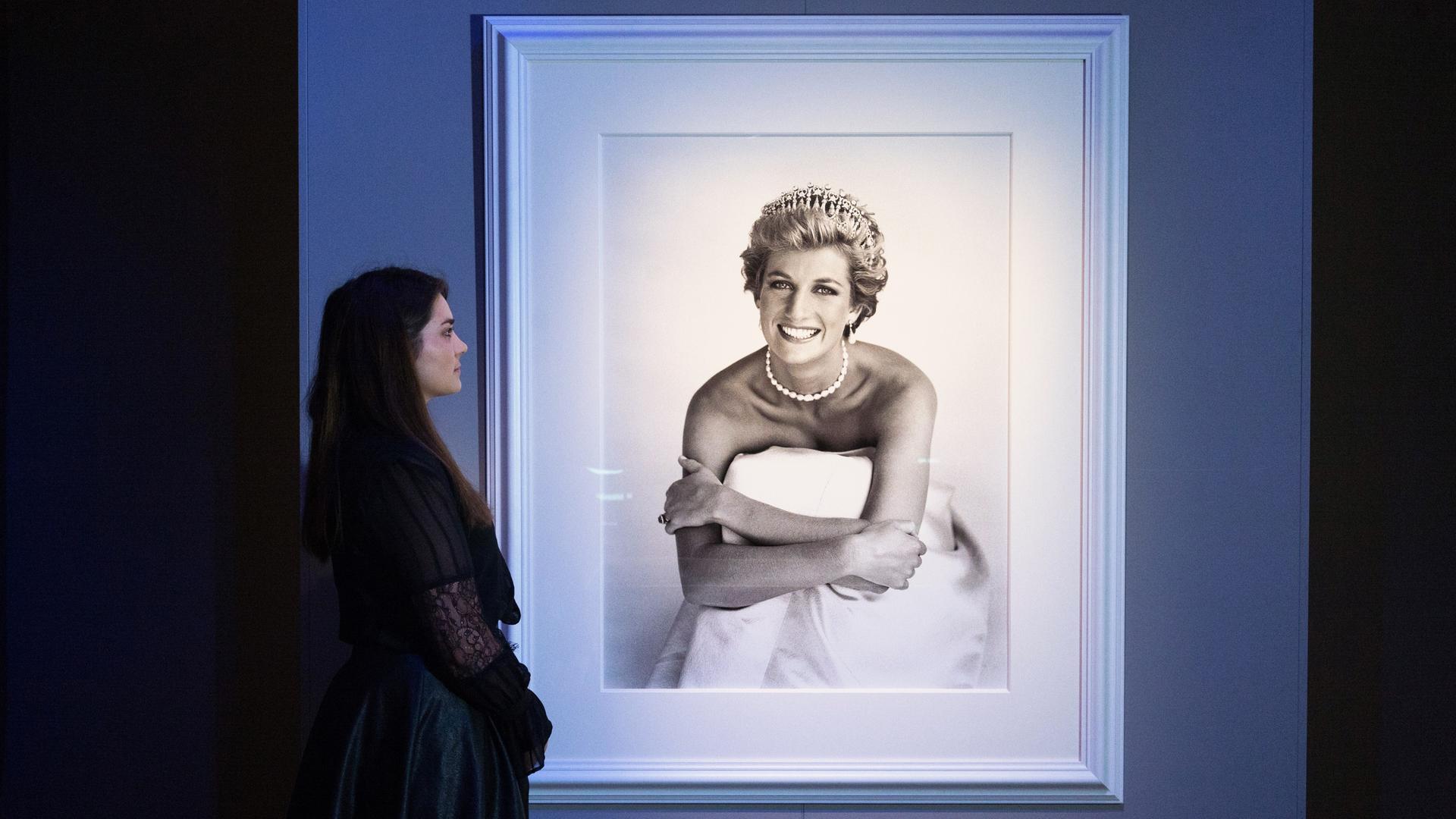 Ein Porträt von Lady Diana aufgenommen von Patrick Demarchelier hängt in einer Ausstellung in London und wird von einer Frau betrachtet.