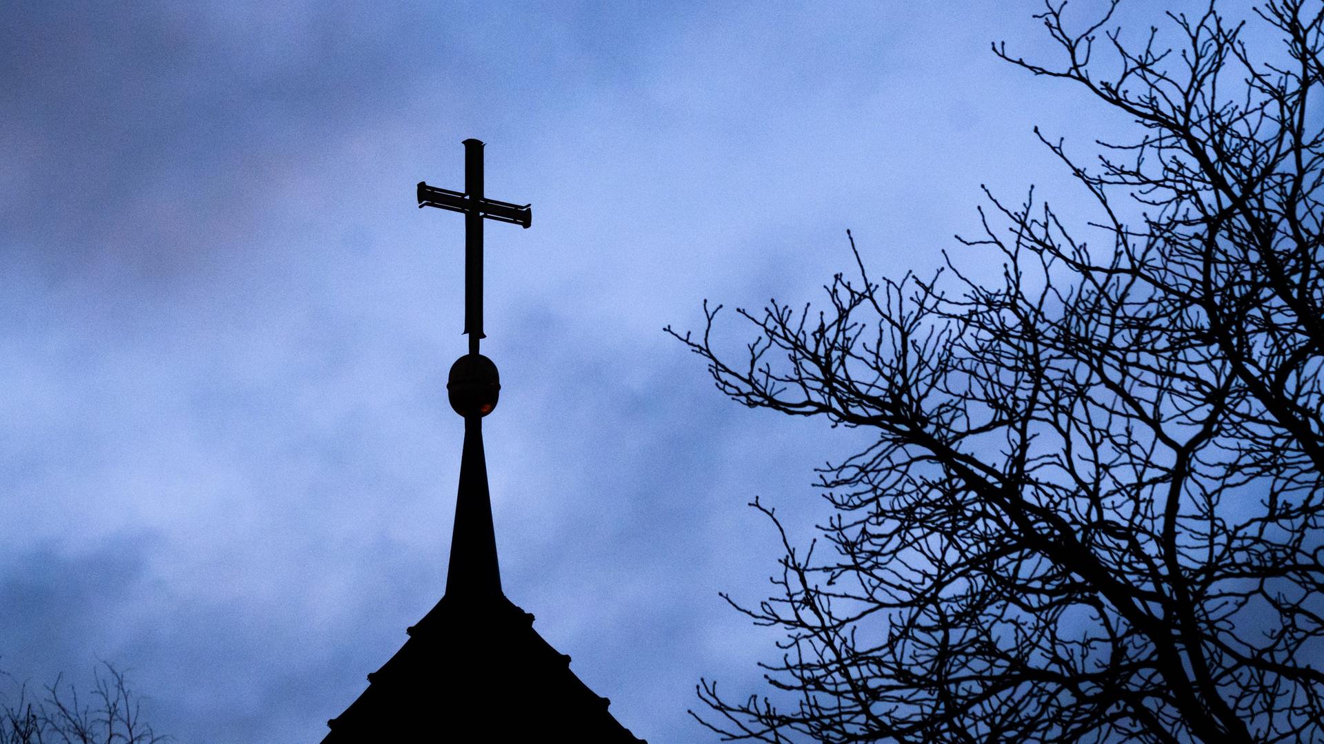 Dunkle Wolken über einem Kirchturm mit Kreuz 