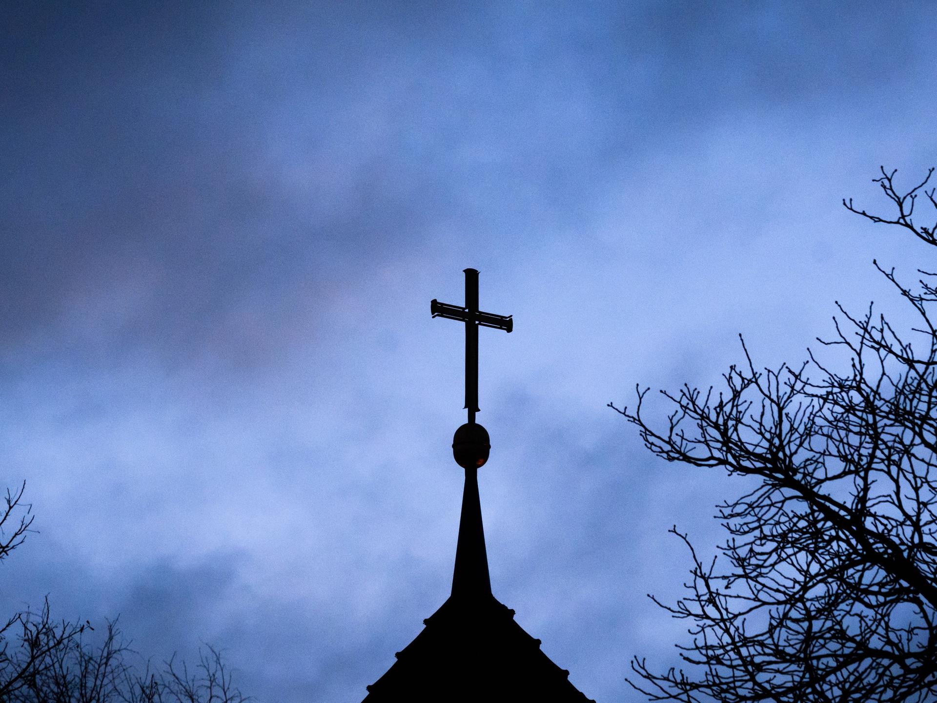 Dunkle Wolken über einem Kirchturm mit Kreuz 