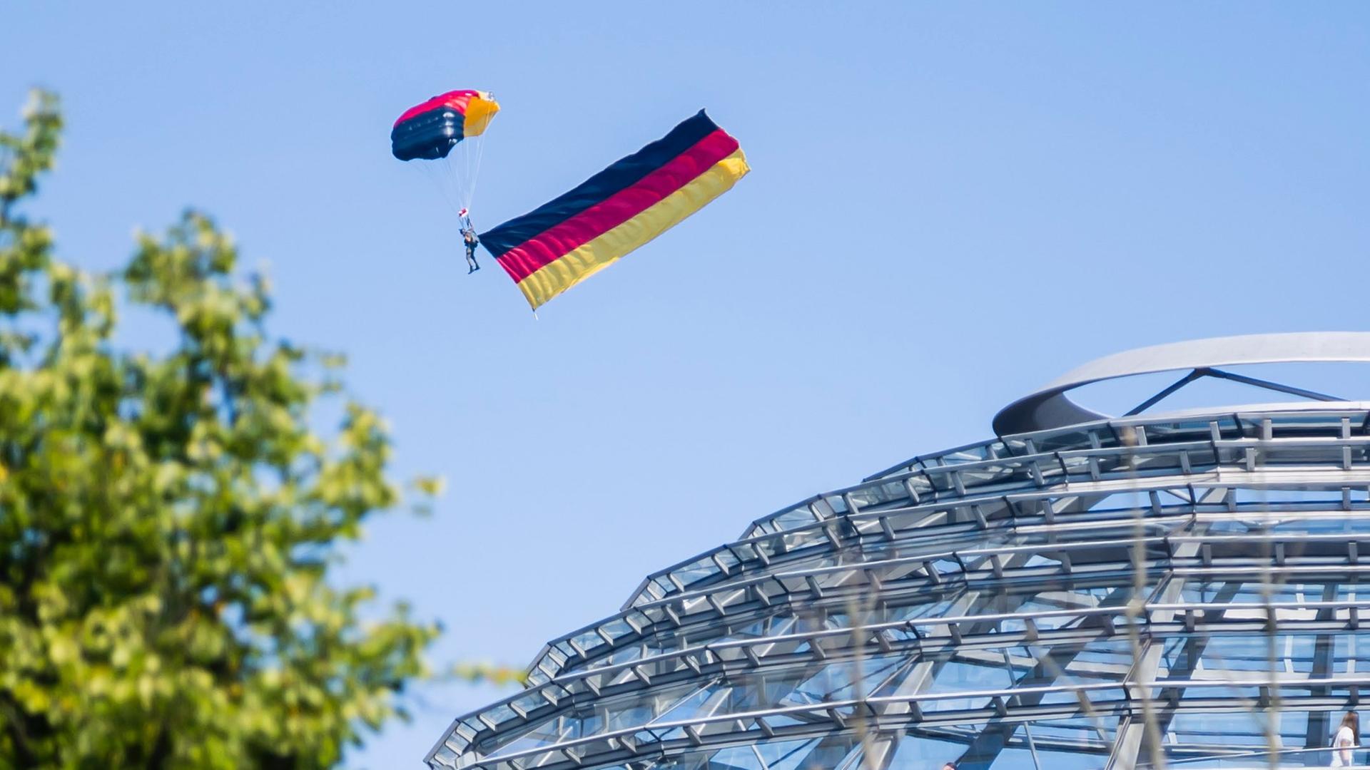 Ein Fallschirmspringer der Bundespolizei fliegt während des Tags der offenen Tür der Bundesregierung über der Kuppel des Reichstagsgebäudes. Ein Fallschirmspringer der Bundespolizei fliegt während des Tags der offenen Tür der Bundesregierung über der Kuppel des Reichstagsgebäudes.