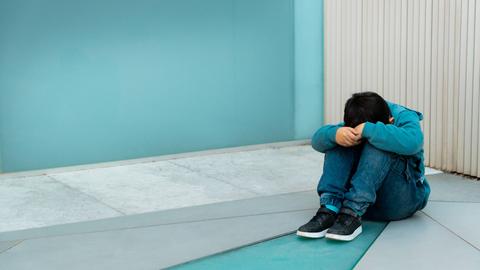 Ein Kind sitzt zusammengekauert in der Ecke, das Gesicht auf den Knien.