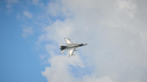 F-16-Kampfjet in der Luft vor blauem Himmel mit Wolken.