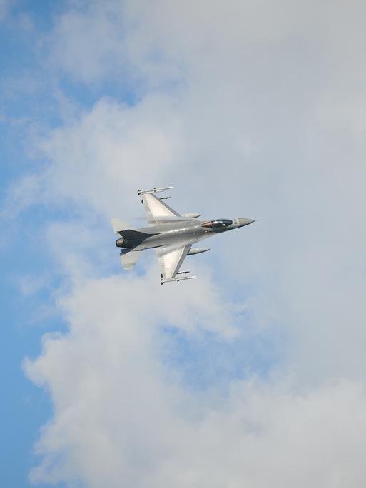 F-16-Kampfjet in der Luft vor blauem Himmel mit Wolken. 