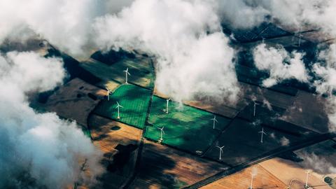 Vogelperspektive auf ein landwirtschaftlich genutztes Feld mit Windrädern.