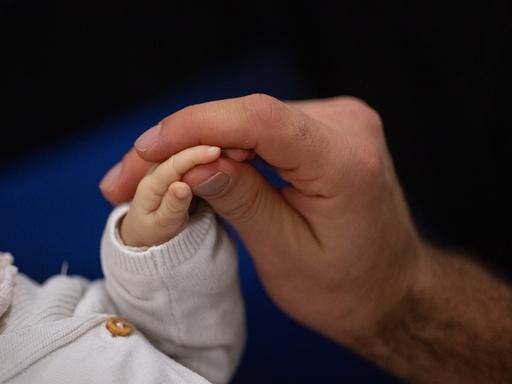 Ein Vater berührt während eines Infant Handling Kurses die Hand seines Kindes. Im Koalitionsvertrag hatten die Regierungsparteien SPD, Grüne und FDP angekündigt, eine zweiwöchige vergütete Freistellung für den Partner oder die Partnerin nach der Geburt eines Kindes einzuführen. Für das Vorhaben kursieren unterschiedliche Begriffe, mal ist von Vaterschaftsurlaub, mal von Väterzeit die Rede - da es meistens Vätern zugutekäme.